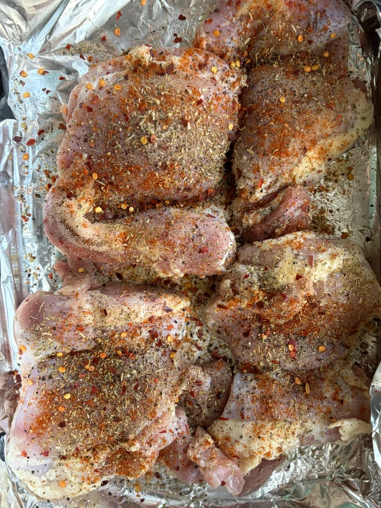 Raw chicken with various seasonings in a foil lined baking dish. 