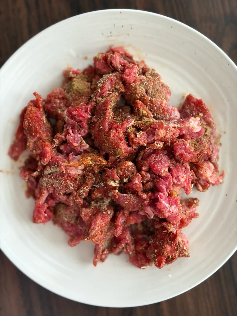Raw steak marinating in spices, sitting on a white plate. 