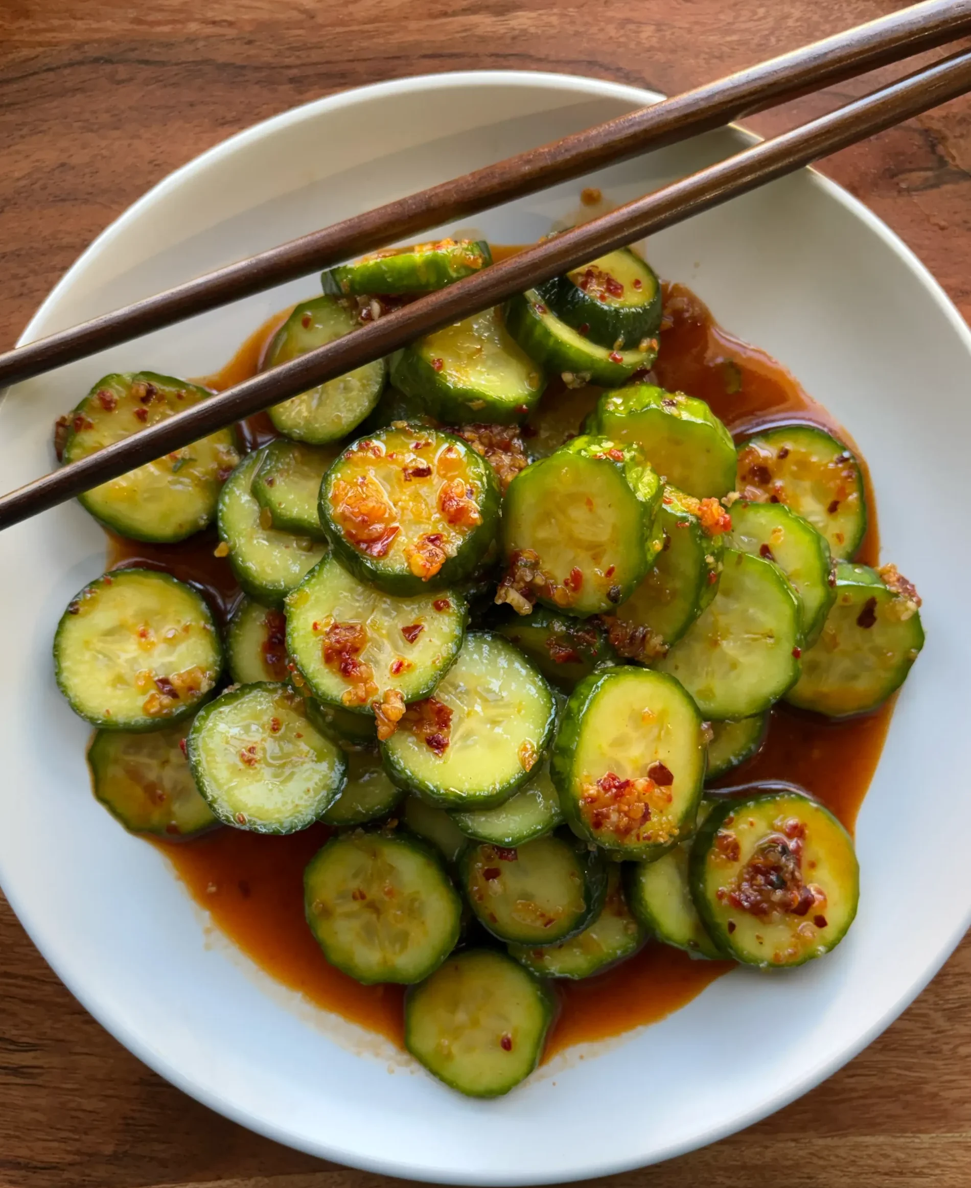 Bowl of spicy cucumbers with chopsticks resting on the bowl.