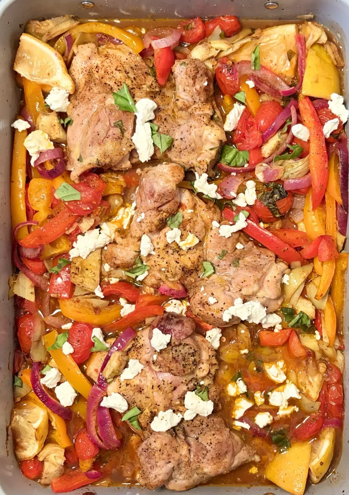 Chicken thighs in a pan cooked alongside bell peppers, red onions, and sprinkled with goat cheese.