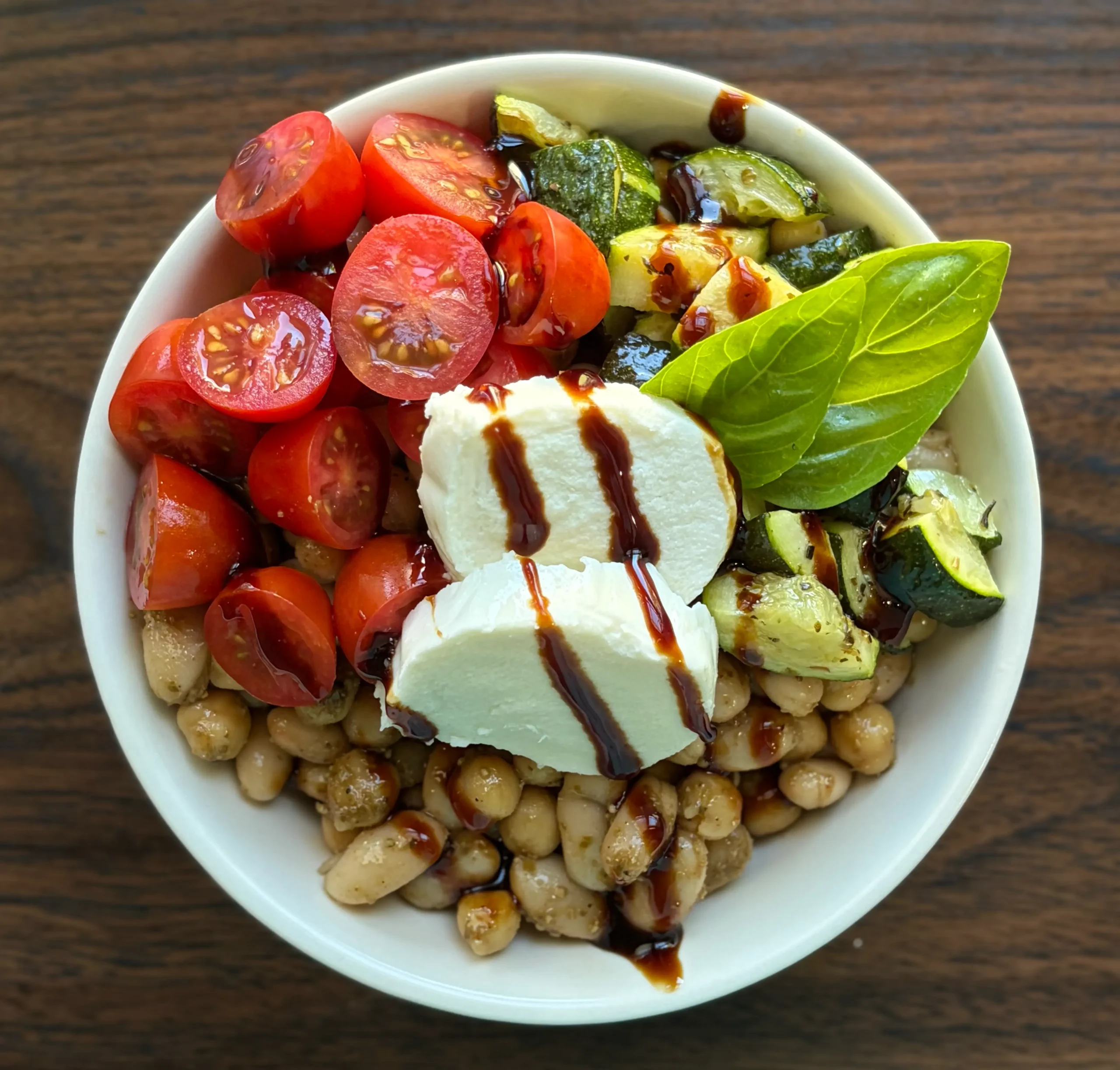 Caprese bean salad topped with cherry tomatoes, baked zucchini, fresh mozzarella and basil with a balsamic glaze drizzled on top. 