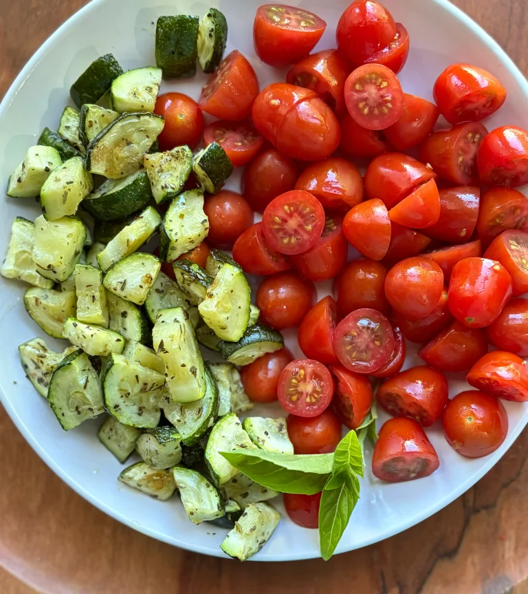 Roasted zucchini with fresh cherry tomatoes on a white plate.