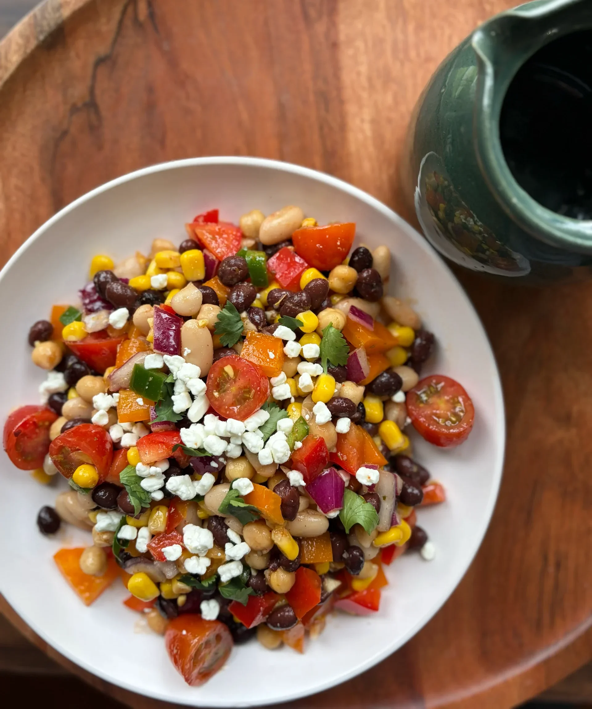 Dense bean salad with vegetables and goat cheese sprinkled on top. A green bowl on the side for decoration.
