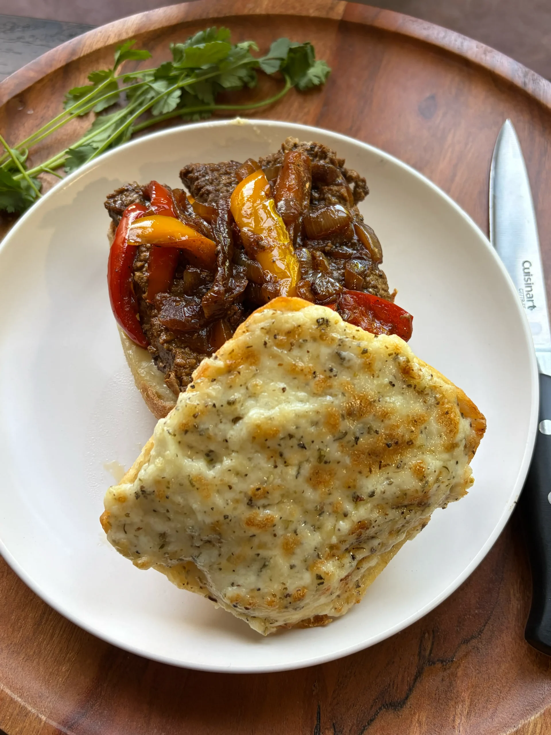 Steak sandwich sitting on a white plate open-faced. Creamy cheese spread on top piece of bread with steak and peppers on the bottom piece of bread. 