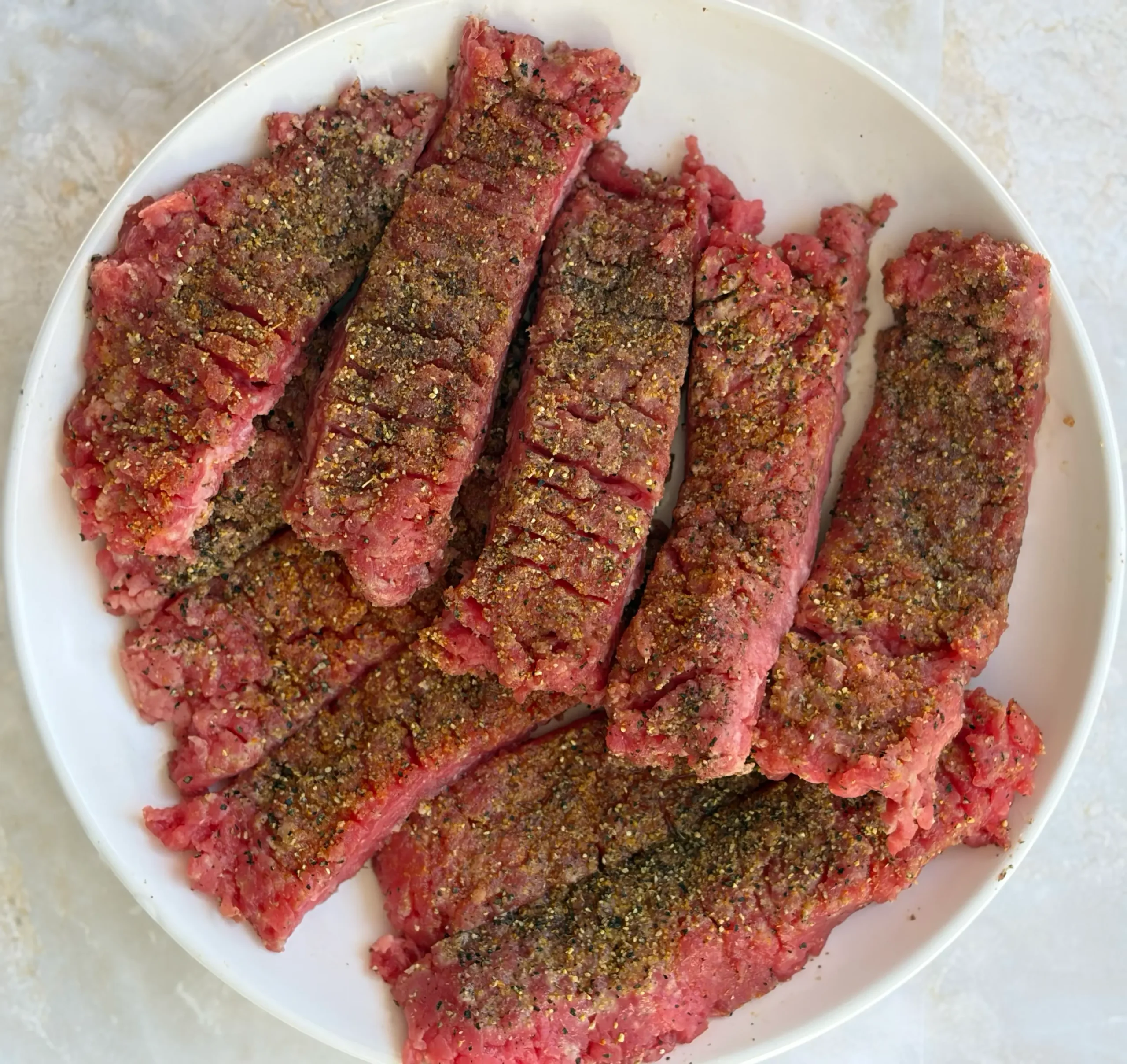 Raw cube steak sliced with seasonings sprinkled on top.