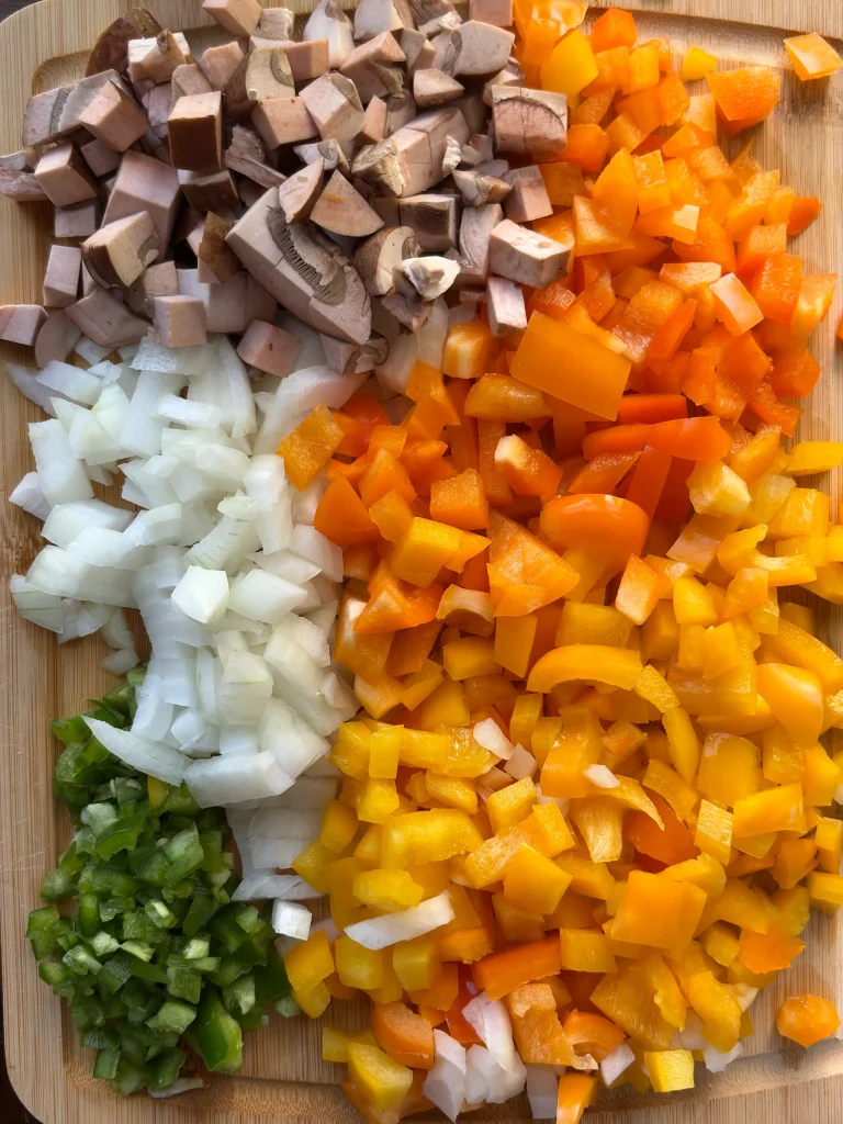 Diced mushrooms, onions, jalapenos, and bell peppers on a wooden cutting board.