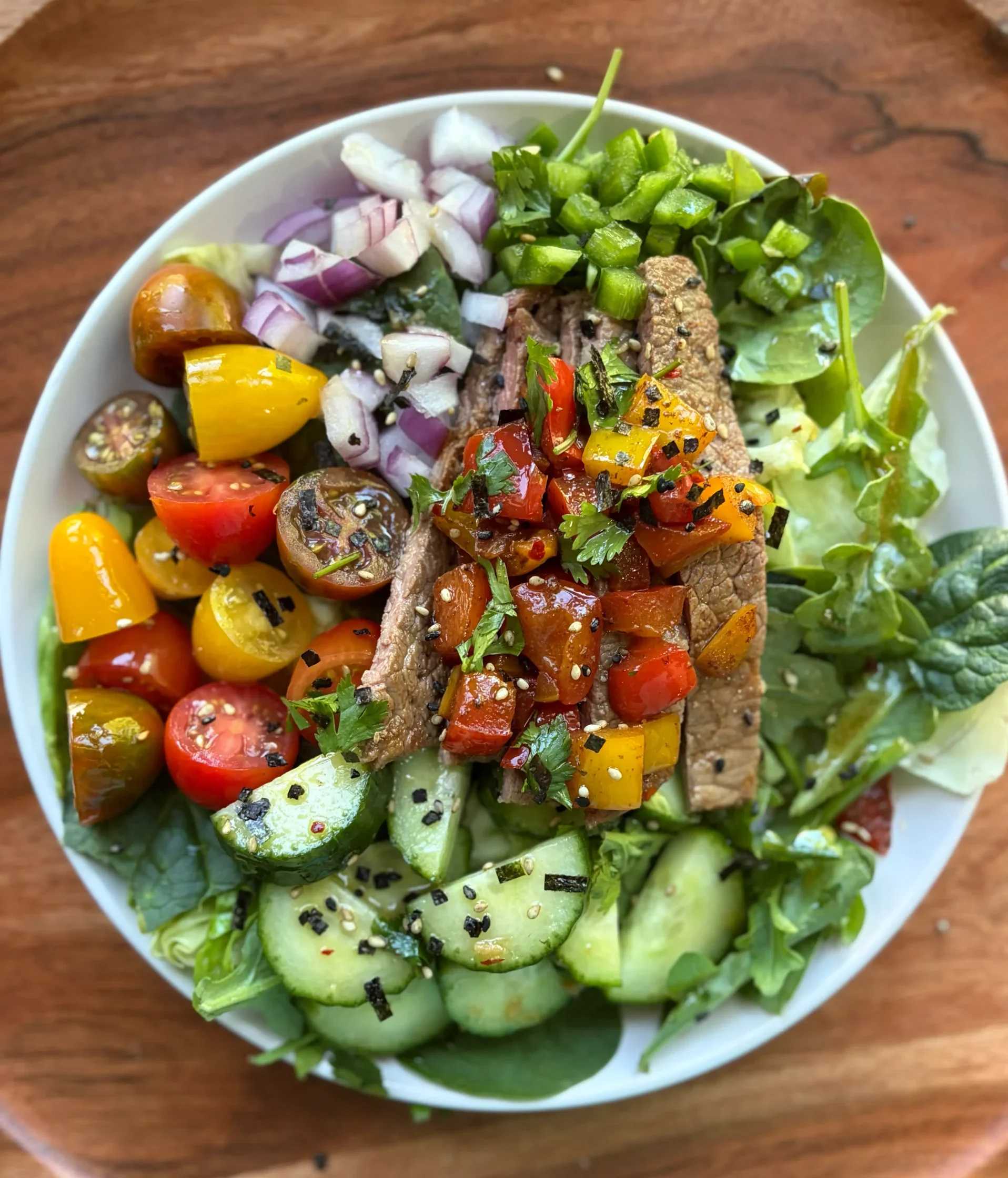 Asian style salad topped with steak, cherry tomatoes, onion and cucumber. Drizzled with salad dressing and topped with grilled peppers. 