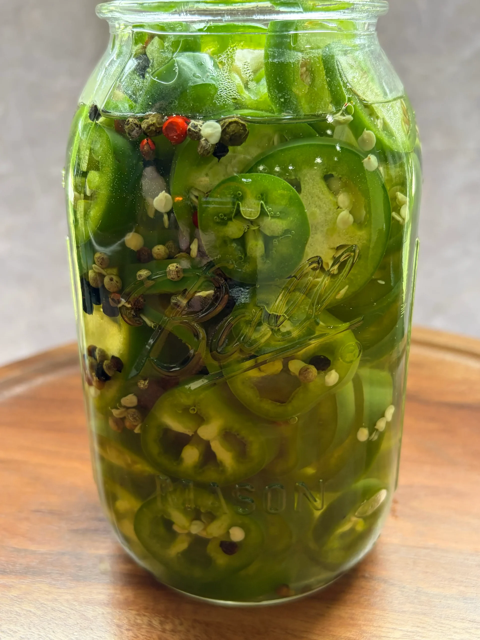 Jalapenos pickling in a mason jar with peppercorns.
