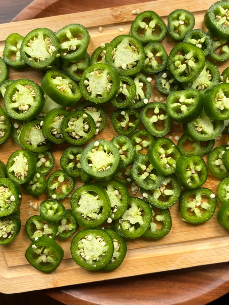 Sliced jalapenos on a wooden cutting board.