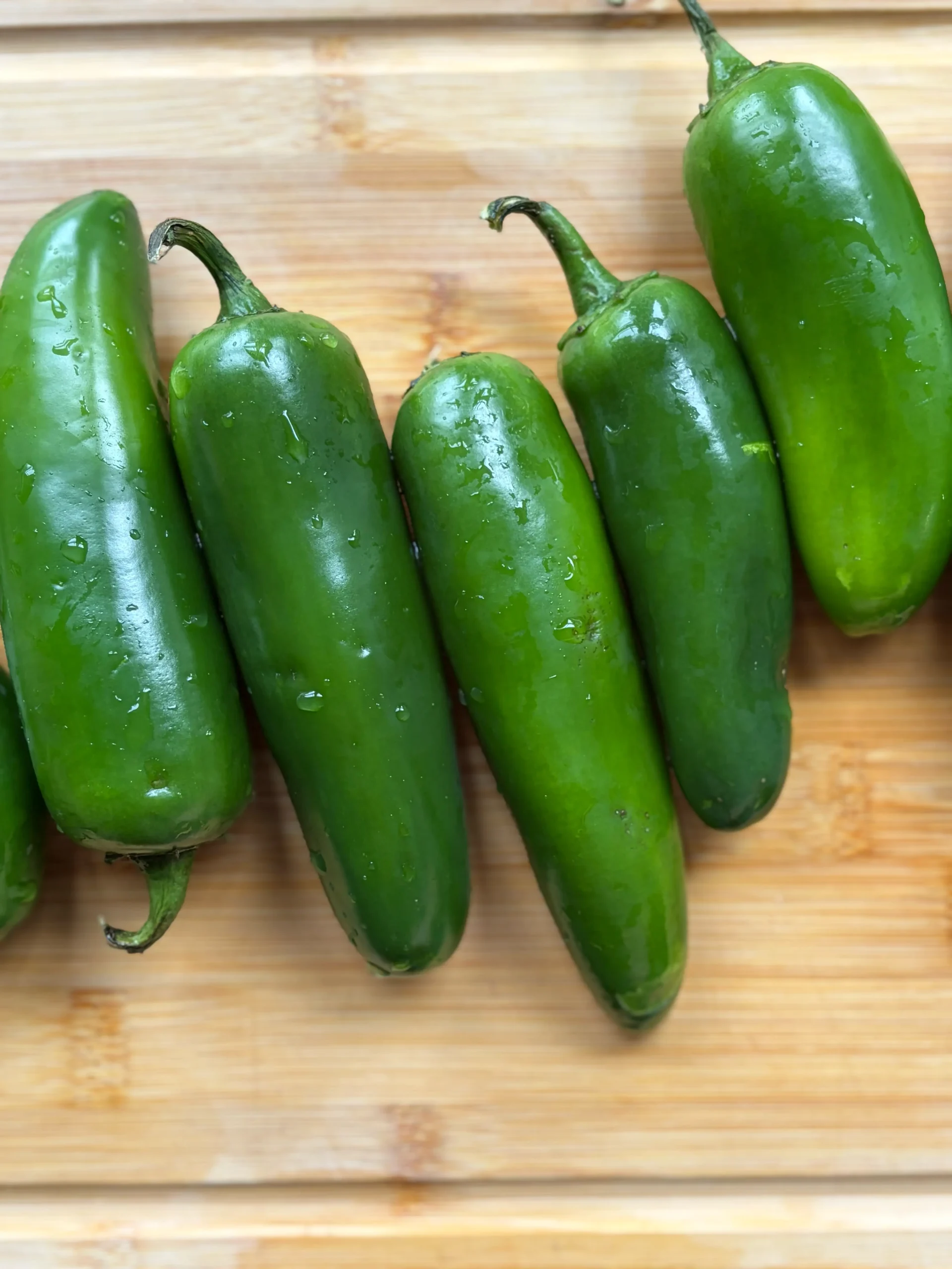 Fresh jalapenos lined up next to each other on a wooden cutting board. 