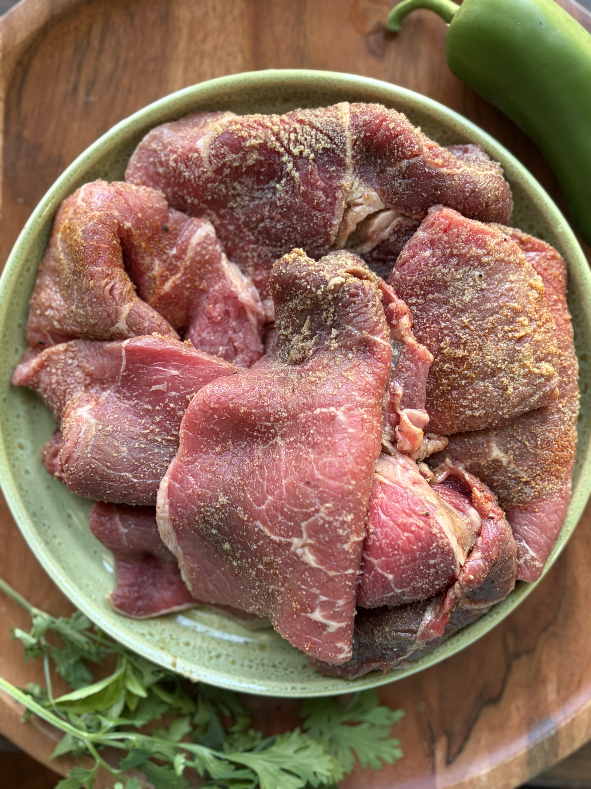 Raw steak with seasonings on a light green bowl.