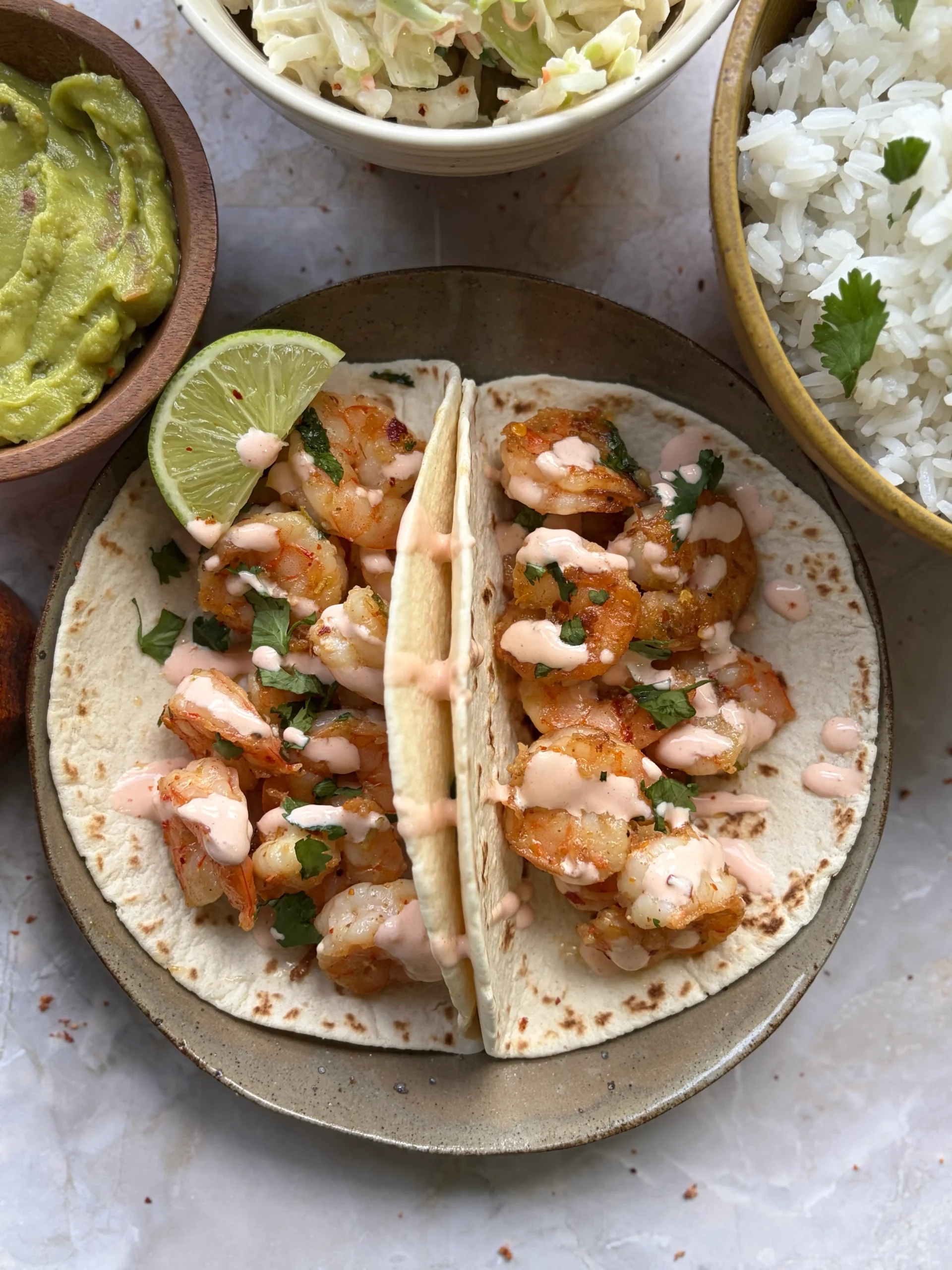 Shrimp tacos on a plate with guacamole, cole slaw, and rice on the side.