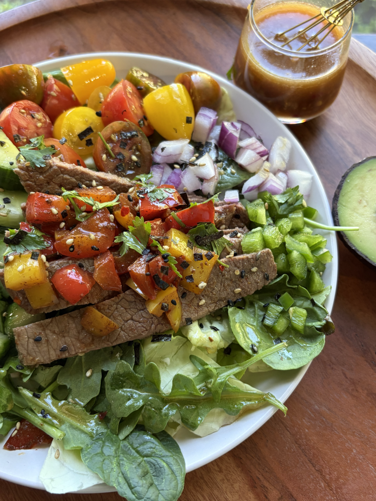 Steak salad on a white plate with a cup of dressing on the side.