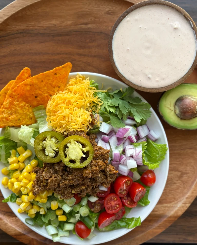 Taco salad with ground beef, corn, cherry tomatoes, cilantro and shredded cheese. Doritos on the side with half of an avocado for garnish with creamy salsa dressing.