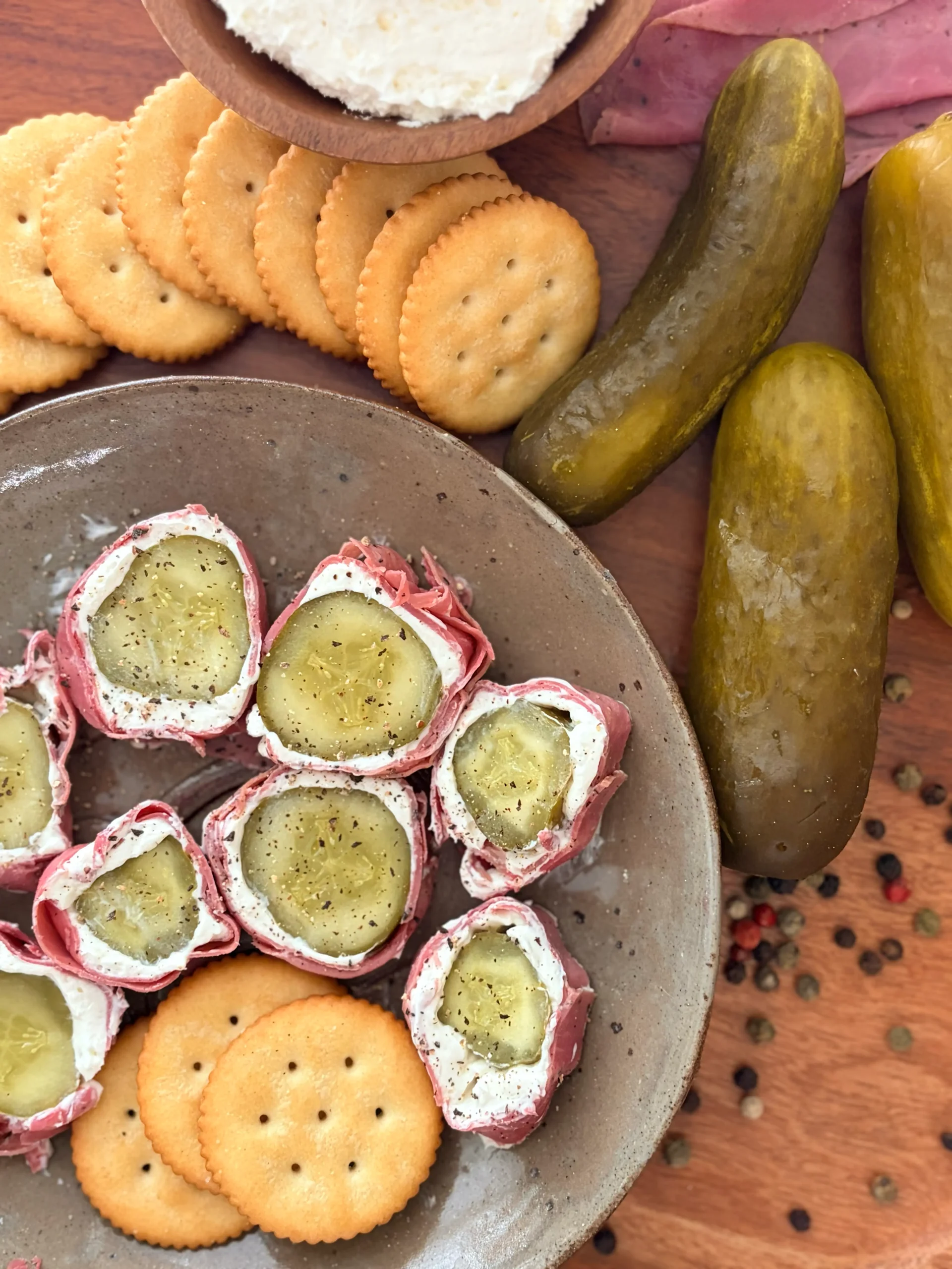 A plate with pickles, cream cheese, and pastrami. Pickles and crackers on the side of the plate for decor. 