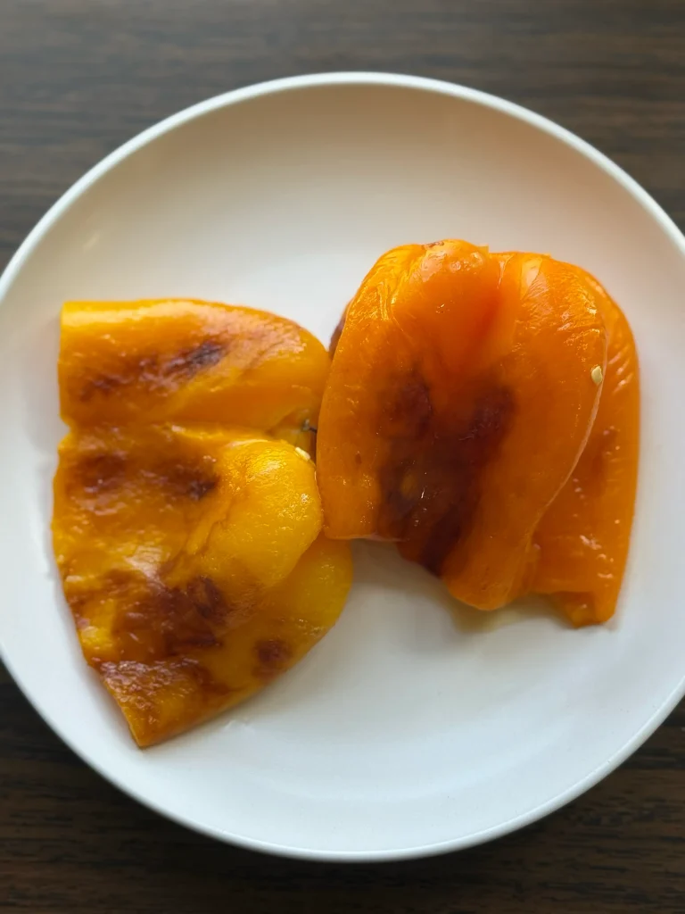 Whole roasted yellow bell pepper and whole roasted orange bell pepper on a white plate.