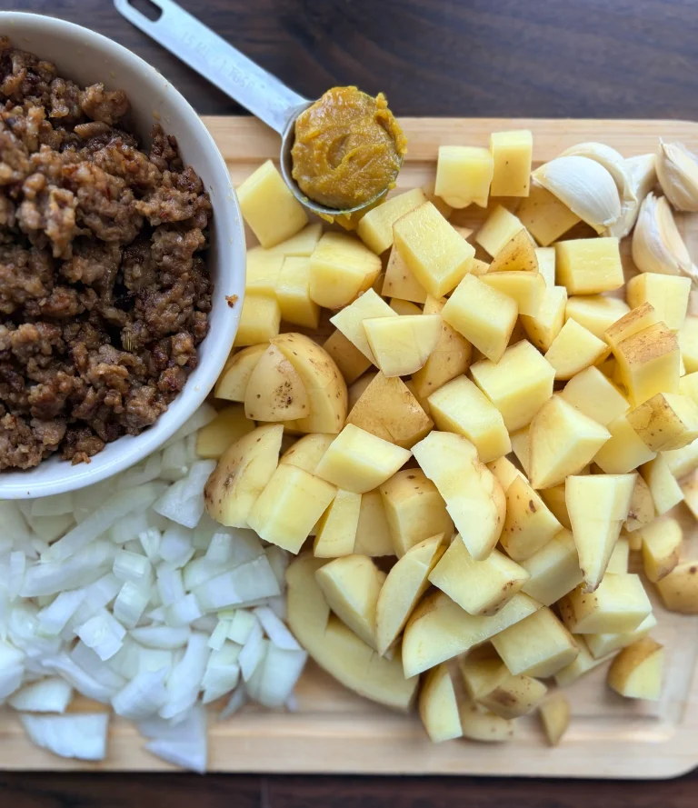 Chopped potatoes, diced white onion, and browned sausage in a bowl.