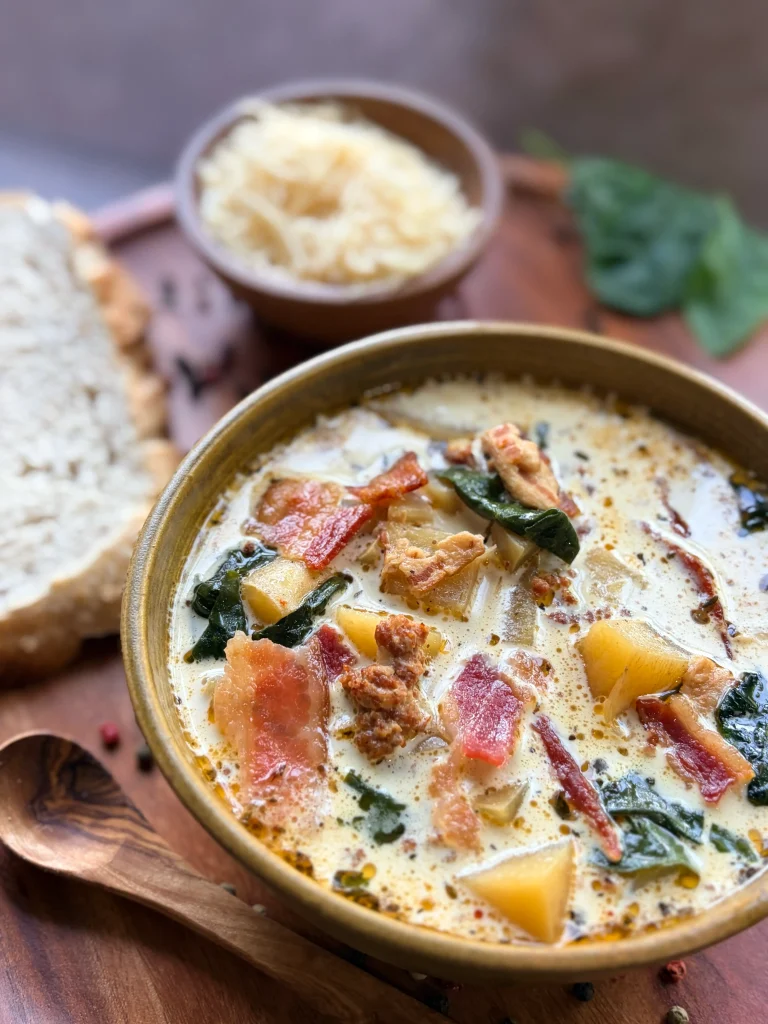 Bowl of zuppa toscana soup with bread and parmesan cheese on the side.