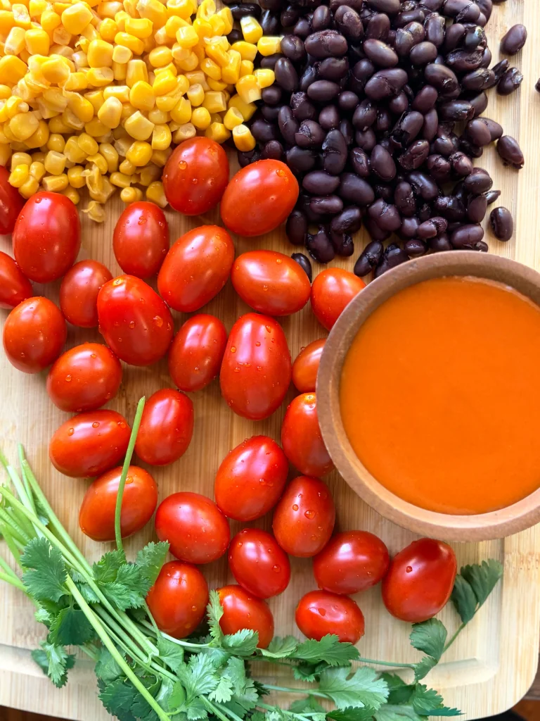 Corn, black beans, and cherry tomatoes on a cutting board. Fresh cilantro on the side.