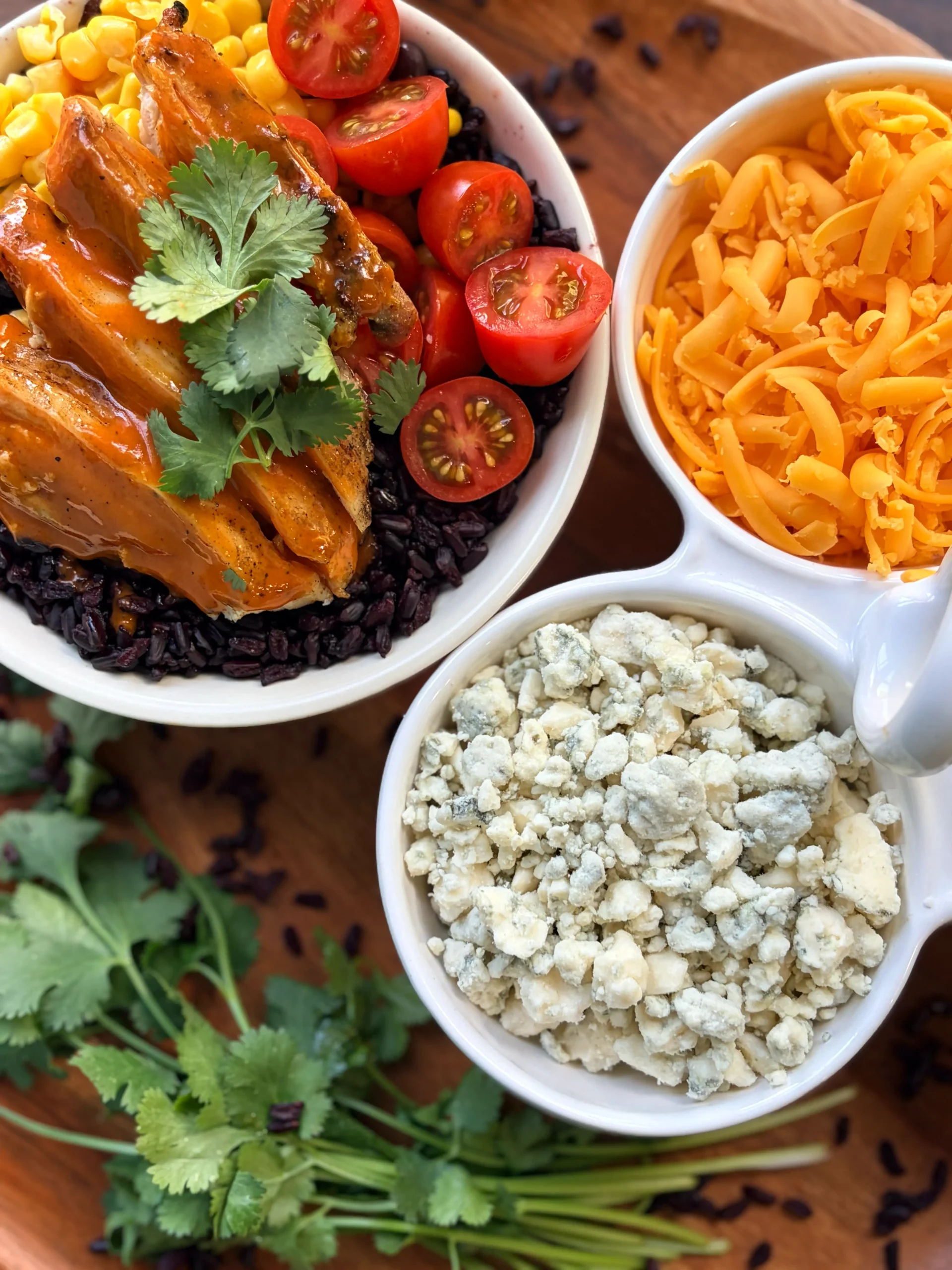 Bowl of buffalo chicken and purple rice. A side of blue cheese and shredded cheddar cheese for topping with fresh cilantro.