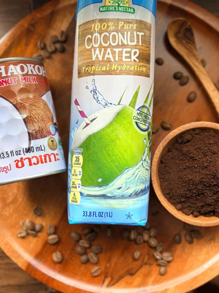 A can of coconut milk, a bottle of coconut water, and ground coffee in a bowl.