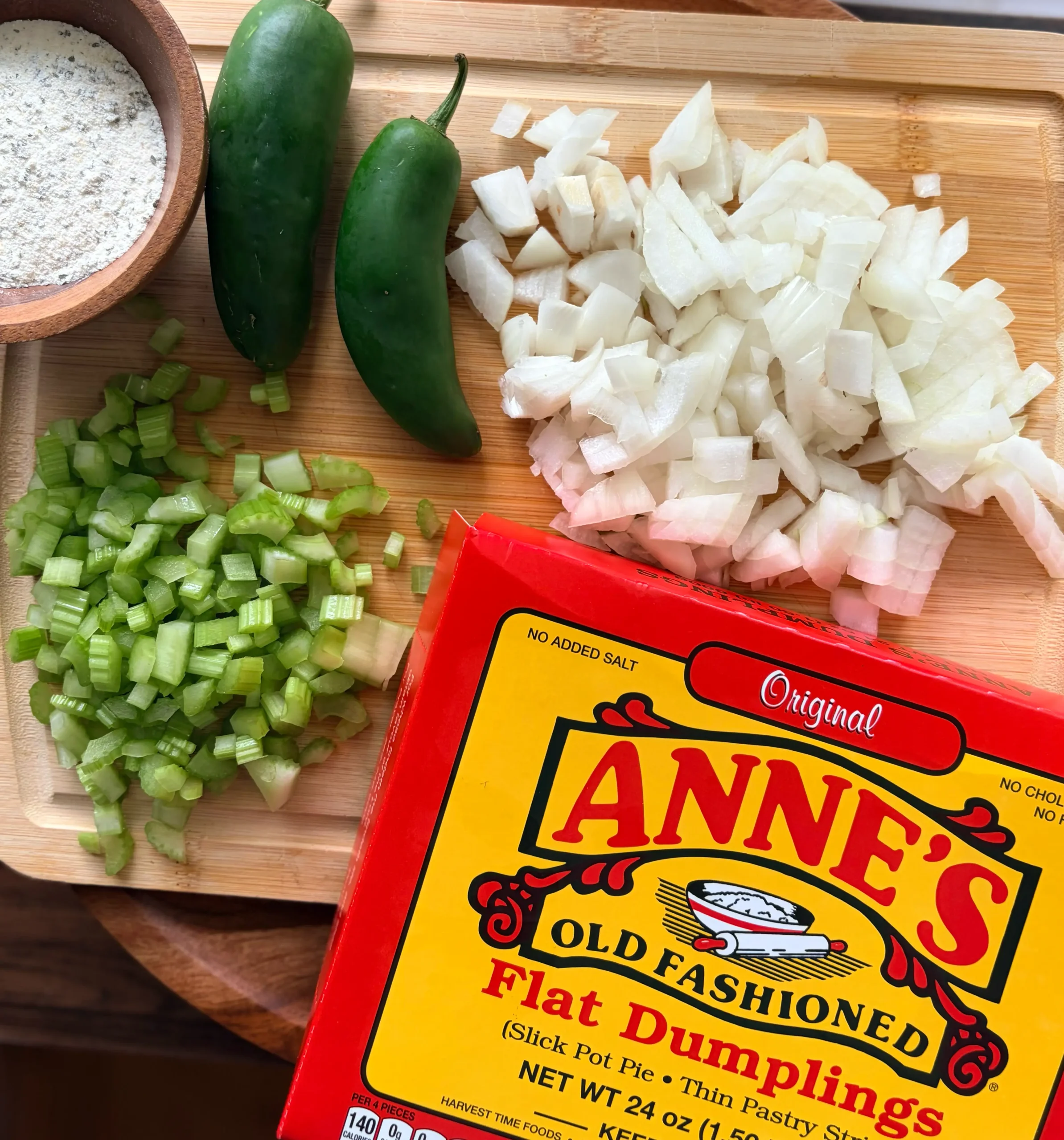 A bowl of ranch seasoning, diced onion, diced celery, and 2 whole jalapenos. Also a package of Anne's old fashioned dumplings on a cutting board.