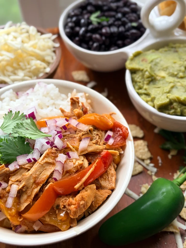 Bowl of chicken and bell peppers. Side of black beans, guacamole, and shredded cheese.