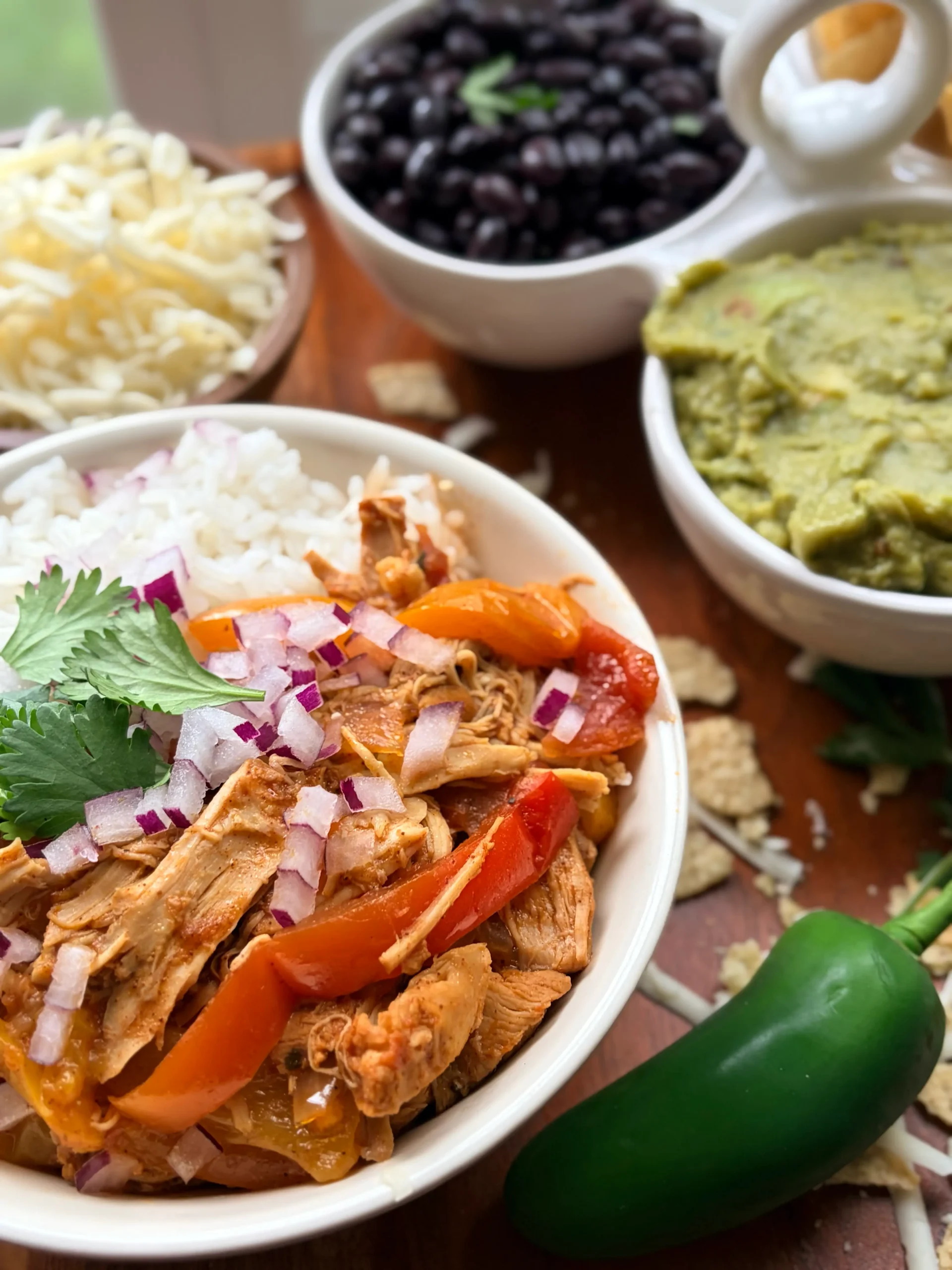 Bowl of chicken and bell peppers. Side of black beans, guacamole, and shredded cheese.