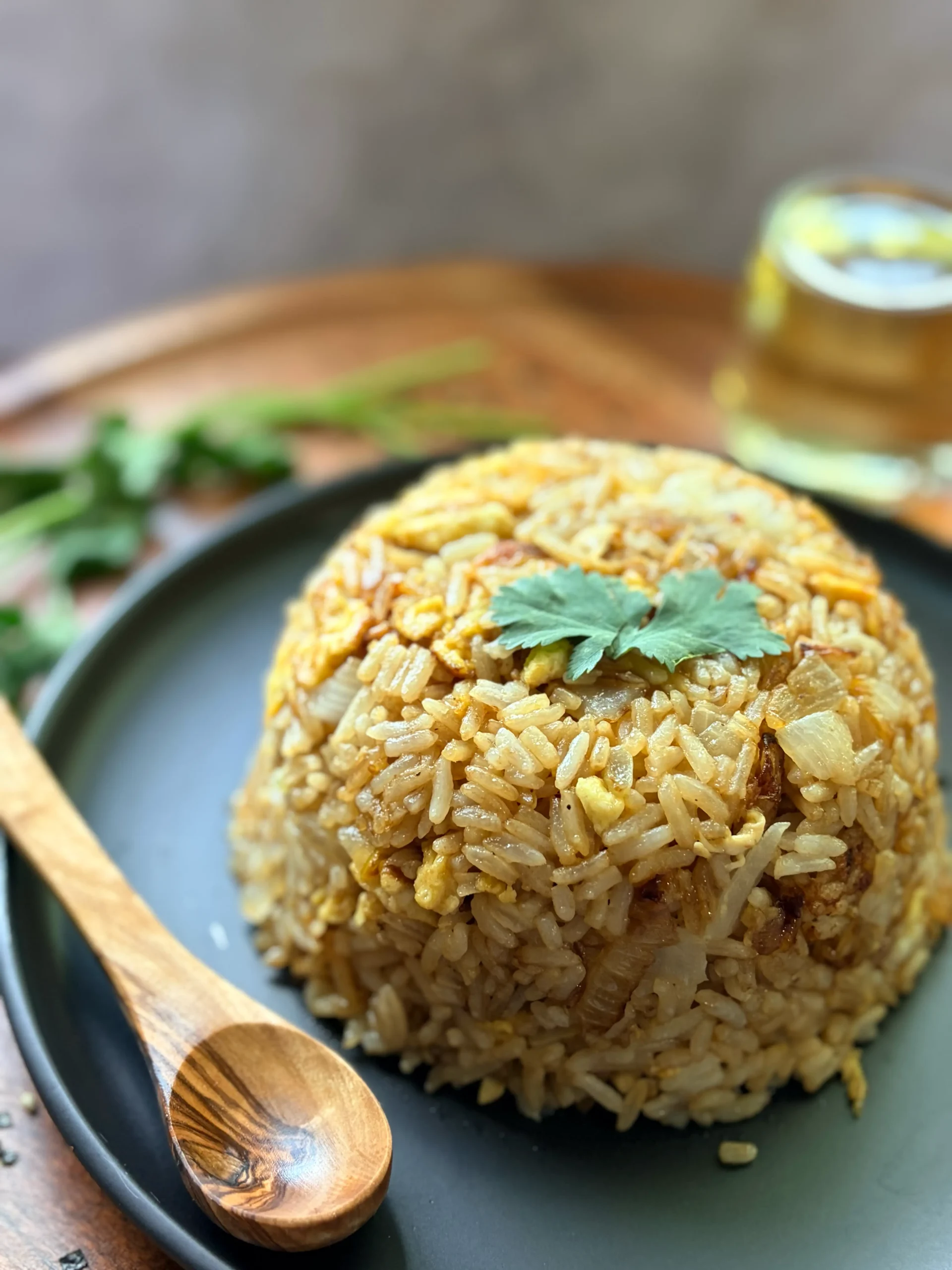 A mound of cooked fried rice and a wooden spoon on a black plate.