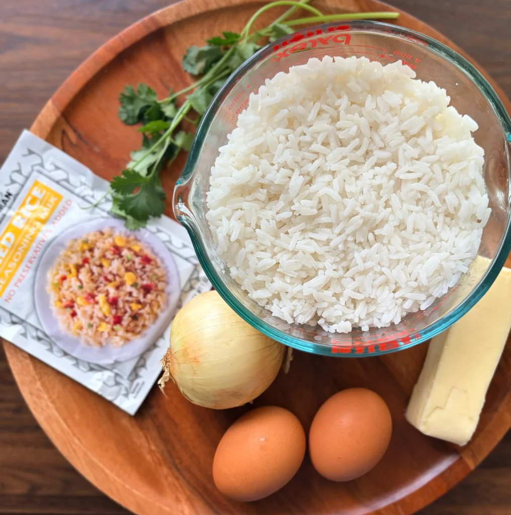 A cup of white rice, 2 eggs, an onion, butter, and fried rice seasoning packet.