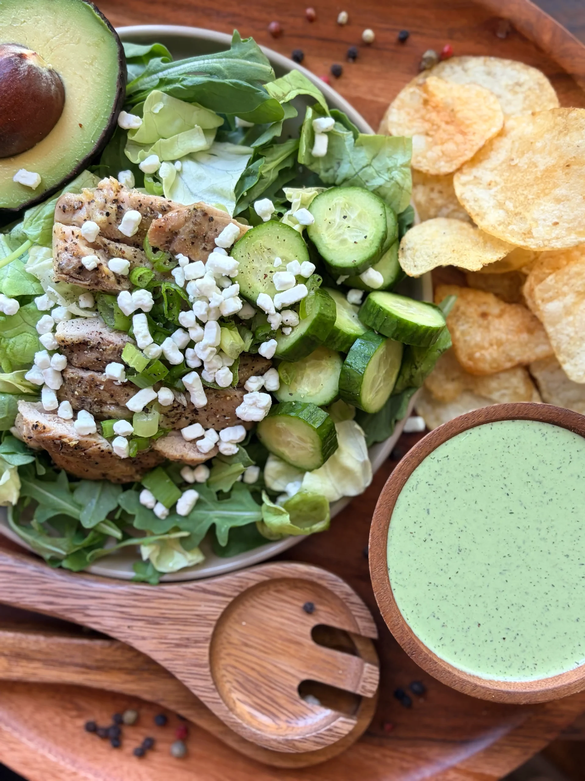 Green salad with an avocado on a plate. Kettle cooked chips on the side with a bowl of green goddess dressing.