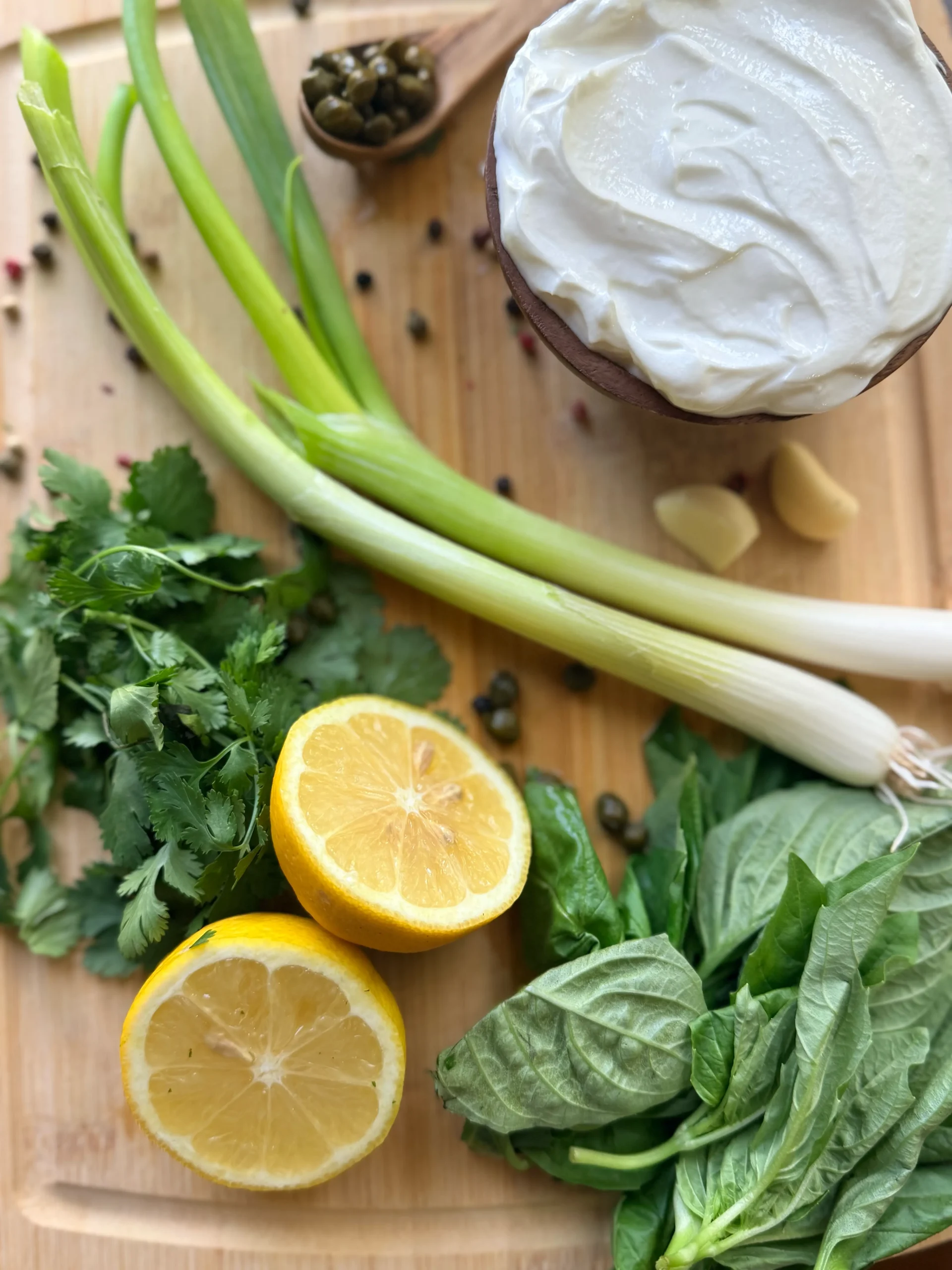 A bowl of greek yogurt, two green onions, a sliced lemon, and fresh herbs.