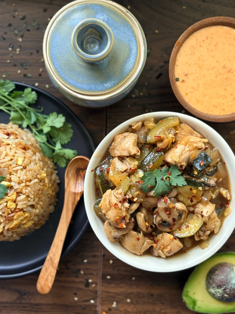 Bowl of hibachi chicken and vegetables with a side of fried rice. Bowl of yum yum sauce and half an avocado on the side.