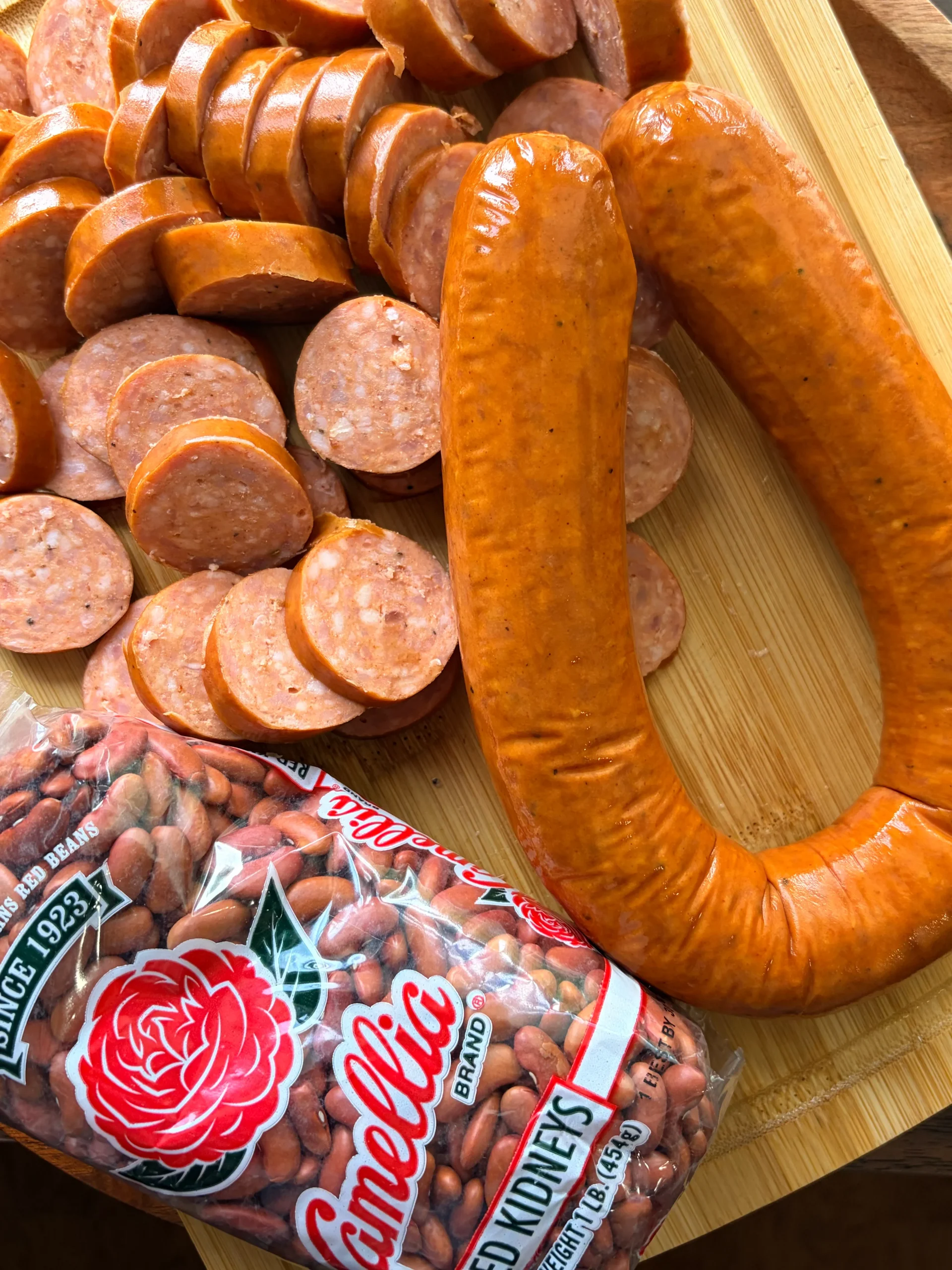Link of sausage whole and one link of sausage diced. A bag of dried kidney beans is sitting beside the sausage.