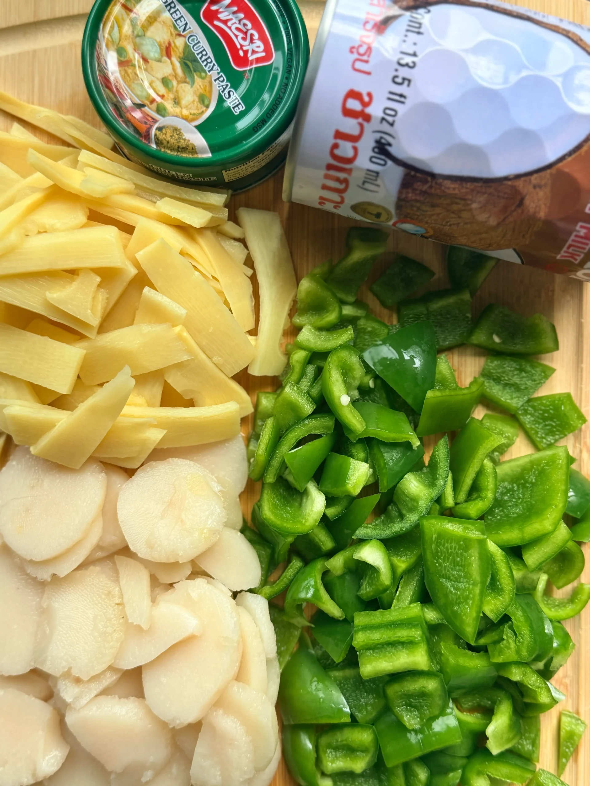 Water chestnuts, bamboo shoots, diced green bell pepper, thai green curry paste, and a can of coconut milk all laying on a cutting board.