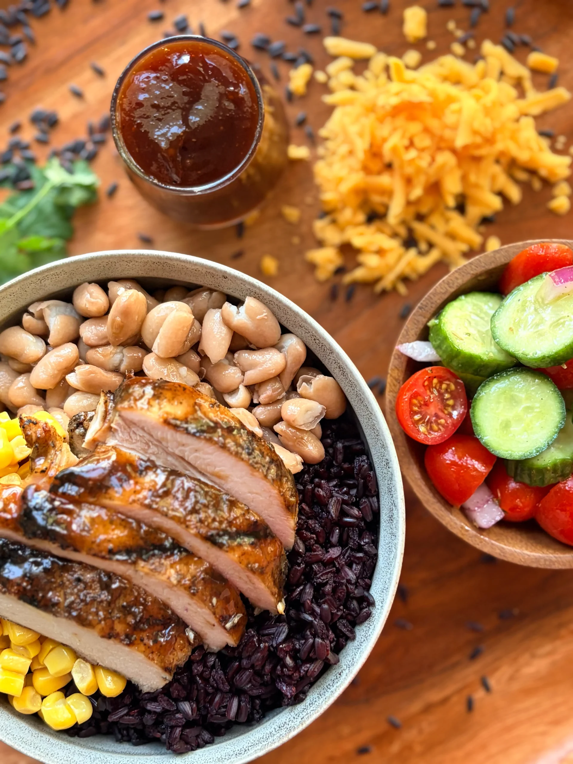BBQ chicken rice bowl with a side of cucumber tomato salad and shredded cheese.