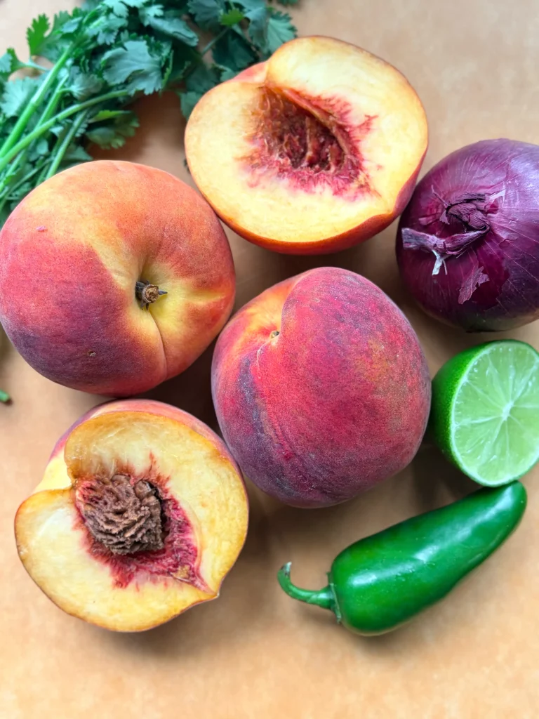 Fresh peaches and a red onion and a half of a lime with a jalapeno for peach salsa.
