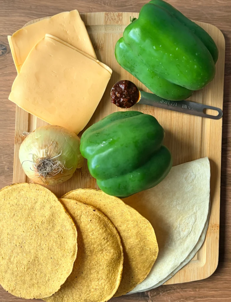 Ingredients for a philly cheesesteak crunchwrap. Two bell peppers, clied cheese, an onion, and tostadas.