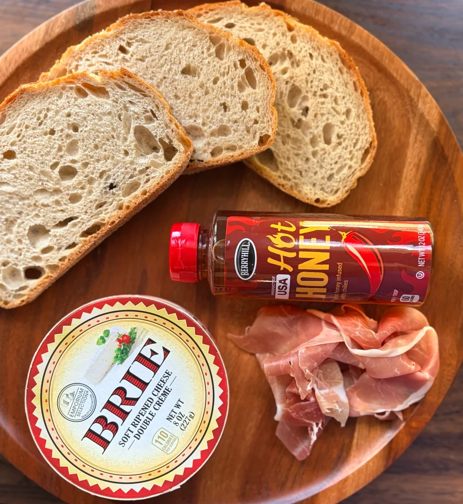 Ingredients for a grilled cheese, prosciutto, brie, hot honey, and bistro bread.
