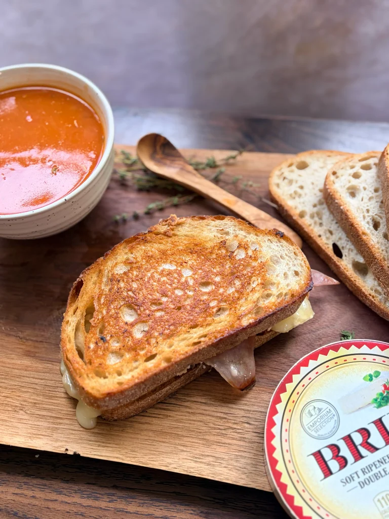 Hot honey brie and prosciutto grilled cheese sandwich with a bowl of tomato soup.