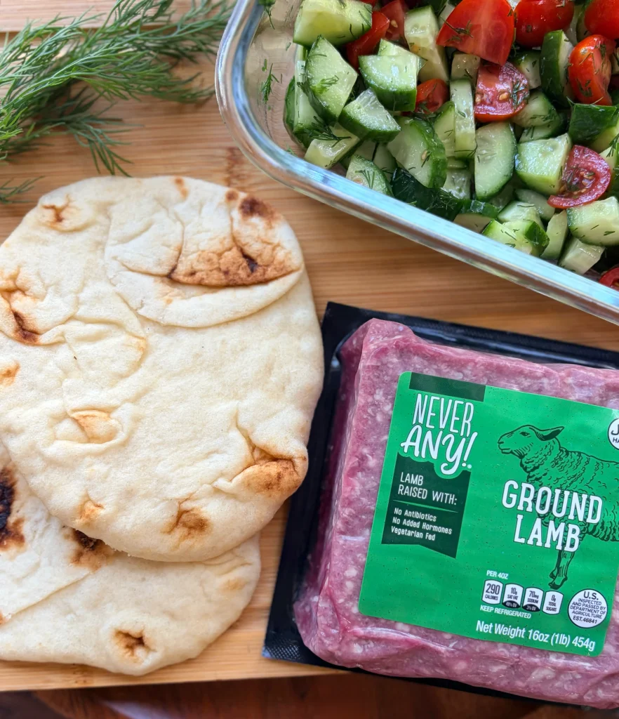 Pita bread, cucumber salad, and ground lamb ingredients for lamb pita dinner.