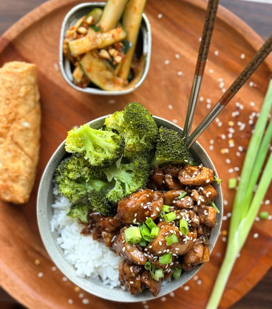 Honey-soy glazed chicken rice bowls with broccoli and an eggroll. Spicy cucumber salad on the side with a green onion sprig for garnish.