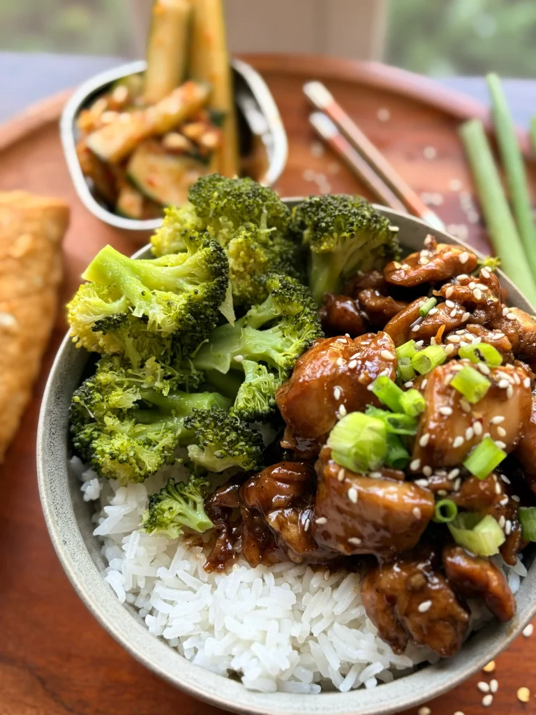 Honey-soy glazed chicken rice bowls with broccoli and an eggroll. Spicy cucumber salad on the side with a green onion sprig for garnish. 